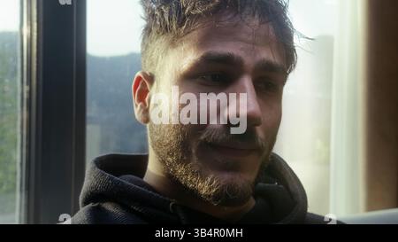 Young Man Looking Concerned While Sitting by the Window in Natural Light Stock Photo