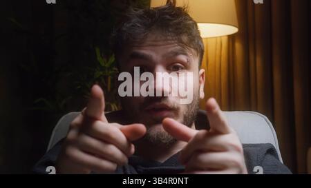 Young male vlogger speaking directly to camera with expressive hand gestures in cozy indoor lighting, creating engaging content for social media Stock Photo
