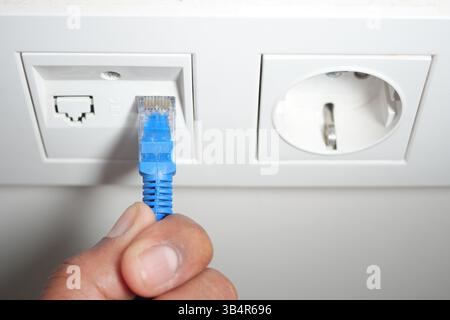 Connecting an ethernet cable to a wall socket in a modern setting Stock Photo