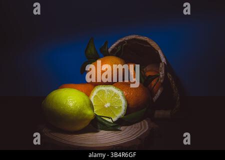A dramatic still life composition of fresh citrus fruits including lemons and tangerines spilling out of a rustic wooden basket. Stock Photo