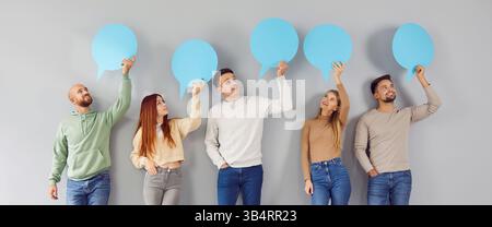 Group of smiling young people holding empty speech bubble in hands on gray background. Stock Photo