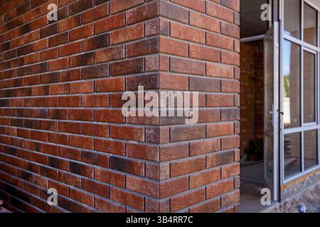 Close-up view of a clean, textured red brick wall corner with an open modern glass door leading into an unfinished interior space Stock Photo