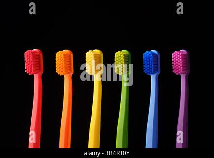 Multicolored plastic toothbrushes on a black background. Banner for dentistry. Colors of the rainbow. Stock Photo