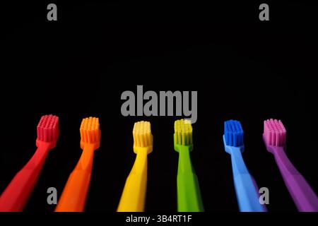 Multicolored plastic toothbrushes on a black background. Banner for dentistry. Colors of the rainbow. Stock Photo