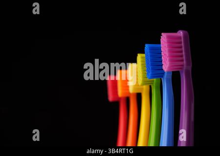 Multicolored plastic toothbrushes on a black background. Rainbow colors. Stock Photo