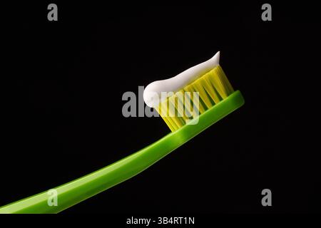 Green plastic toothbrush with white toothpaste on a black background. Professional photo. Stock Photo