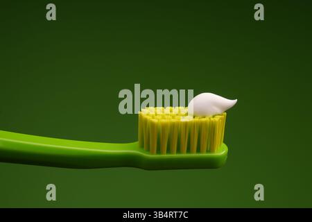 Green plastic toothbrush with white toothpaste on a green background. Oral health. Stock Photo