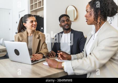 Business team discussing project during a meeting in modern office using laptop, taking notes and smiling Stock Photo