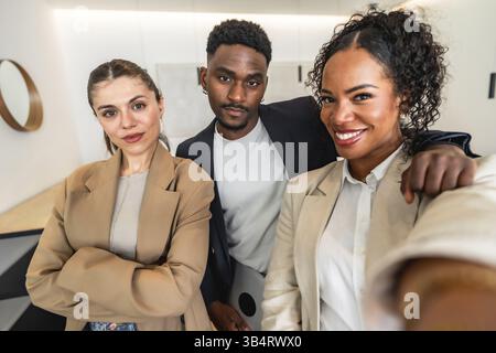 Three smiling businesspeople are taking a selfie in a modern office, showing teamwork and collaboration Stock Photo