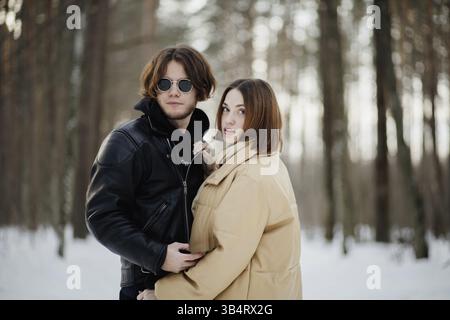 A couple embraces in a quiet snowy forest, surrounded by trees and a tranquil setting Stock Photo