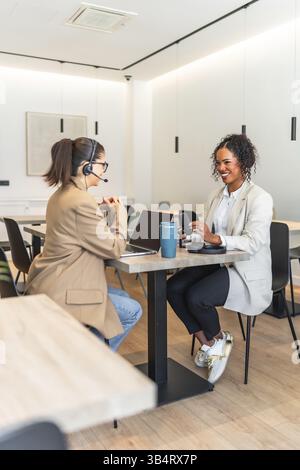 Two female podcasters are recording a new episode in a modern office, using a microphone and laptop Stock Photo
