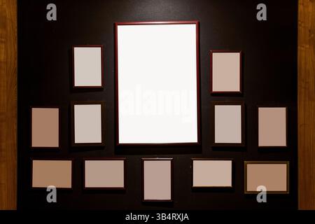 Collection of various sized blank wooden photo frames arranged on a black wall, creating a minimalistic and artistic display ready for custom artwork Stock Photo