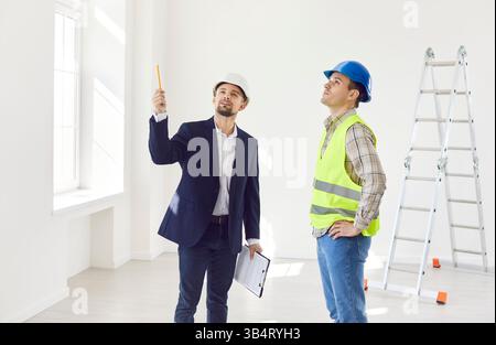 Engineer standing with foreman in room, pointing at something, consulting about renovation, design. Stock Photo