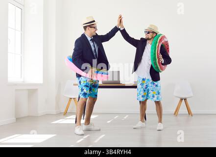 Funny workers standing in office with rubber ring giving high five going on holiday trip. Stock Photo