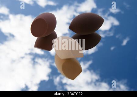 White clouds are visible in the reflection. Fashion photo. Makeup tools. Three sponges of different shapes and colors lie on the glass. Stock Photo