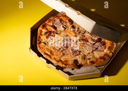 Pizza with sausage and mushrooms. Pizza in a delivery box you can put your letter on a yellow background. Stock Photo