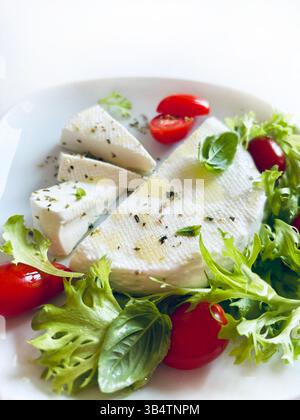 "Primosale", typical sicilian pecorino cheese. Fresh cheese with vegetables and basil leaf, olive oil on a white plate white background. Stock Photo