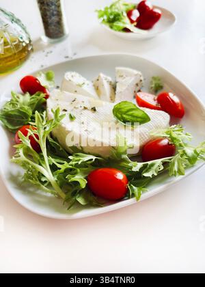 "Primosale", typical sicilian pecorino cheese. Fresh cheese with vegetables and basil leaf, olive oil on a white plate, on white background. Directly Stock Photo