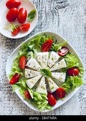 "Primosale", typical sicilian pecorino cheese. Fresh cheese with vegetables and basil leaf, olive oil on a white plate, on wooden background. Directly Stock Photo