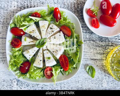 "Primosale", typical sicilian pecorino cheese. Fresh cheese with vegetables and basil leaf, olive oil on a white plate wooden background. Stock Photo