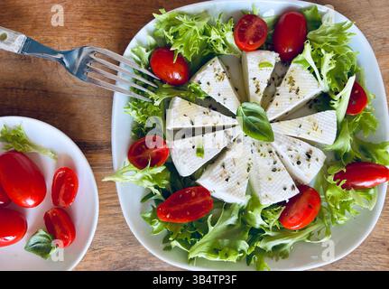 "Primosale", typical sicilian pecorino cheese. Fresh cheese with vegetables and basil leaf, olive oil on a white plate wooden background. Stock Photo