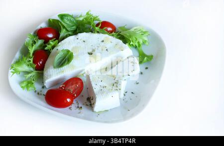 "Primosale", typical sicilian pecorino cheese. Fresh cheese with vegetables and basil leaf, olive oil on a white plate, on white background. Directly Stock Photo