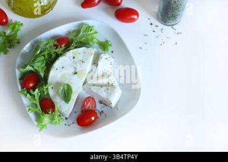 "Primosale", typical sicilian pecorino cheese. Fresh cheese with vegetables and basil leaf, olive oil on a white plate white background. Stock Photo