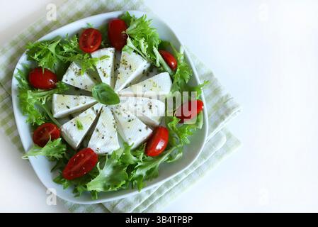 "Primosale", typical sicilian pecorino cheese. Fresh cheese with vegetables and basil leaf, olive oil on a white plate, on white background. Stock Photo
