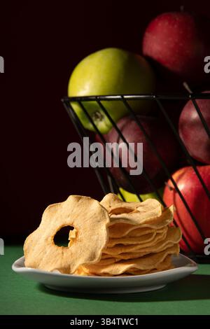 Dried apples on a white plate. Behind is a basket of apples. Studio photo on a dark background. Stock Photo