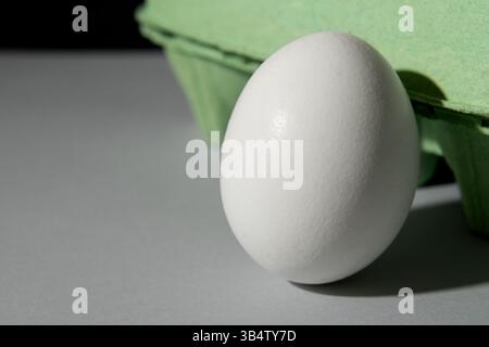 Cardboard green egg box on a gray background, one egg is outside the box. Stock Photo