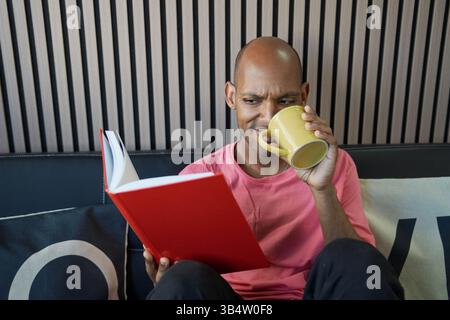 Man enjoying a quiet moment reading a book and drinking coffee, immersed in literature and relaxation Stock Photo