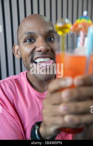 Playful bald man sticking out his tongue while holding a refreshing orange cocktail Stock Photo