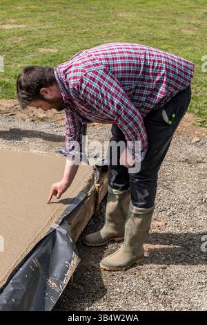 A builder follows the old custom of burying money in the foundations of a new building, for luck, by pushing a pound coin into the wet concrete slab Stock Photo