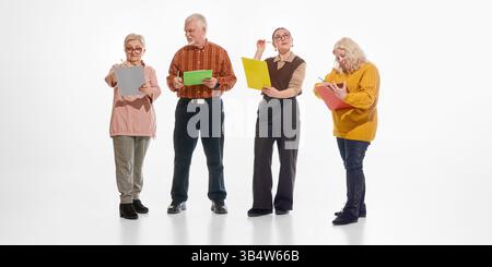 Group of senior students standing and writing, taking notes, on colorful clipboards against white studio background. Active minds in mature age. Stock Photo