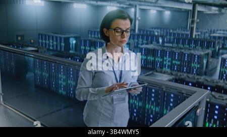 Big Data Center with Server Racks: Female Administrator Using Tablet Computer, Activating Servers Standing In Warehouse. Concept of Information Technology, Machine Learning, Web Service. Medium Shot. Stock Photo