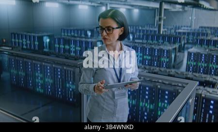 Big Data Center with Server Racks: Female Administrator Using Tablet Computer, Activating Servers Standing In Warehouse. Concept of Information Technology, Machine Learning, Web Service. Medium Shot. Stock Photo