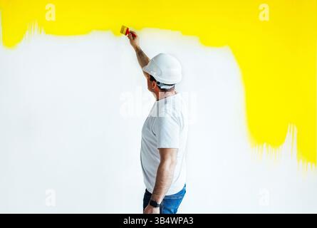 Professional painter paints wall with brush to the yellow color. Decoration and improvement office interior concept Stock Photo