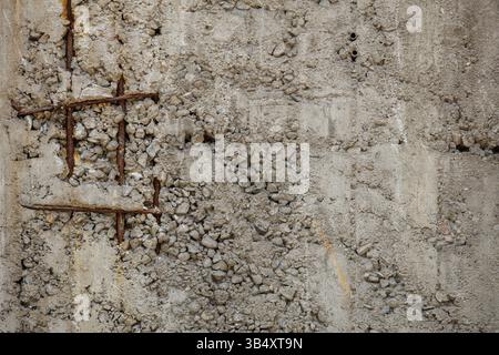 Rusted rebar grid protrudes from unfinished, weathered concrete wall, forming orange brown hued tic-tac-toe matrix on monotone gray surface texture. Stock Photo