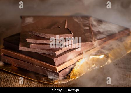 Stack of artisanal dark and milk chocolate bars and pieces, placed on top of each other, surrounded by smoke. Stock Photo