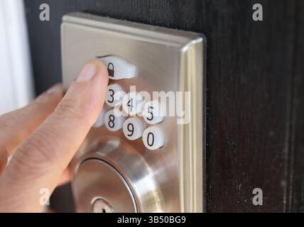 Person using electric door keypad, close up. Finger on keyless door access number pad installed on black door. Used for coded access to open doors wit Stock Photo
