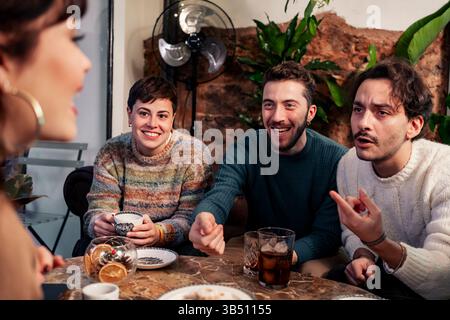 Group of diverse young adults having fun conversation over drinks in a cozy cafe atmosphere, enjoying social connection and laughter Stock Photo