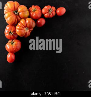 Assorted heirloom and cherry tomatoes arranged on black rustic background, ideal for healthy eating and culinary concepts with copy space Stock Photo