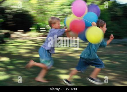 Boys in garden running with party balloons. Stock Photo