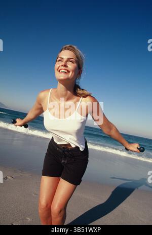 Young woman fitness training with weights at the beach. Stock Photo
