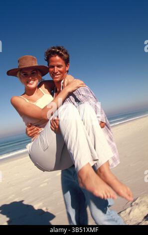 Lifestyle. Happy young couple at the beach. Man carrying woman. Stock Photo