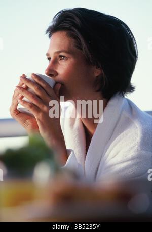 Outdoor profile of young woman in bathrobe holding a cup of hot drink. Stock Photo