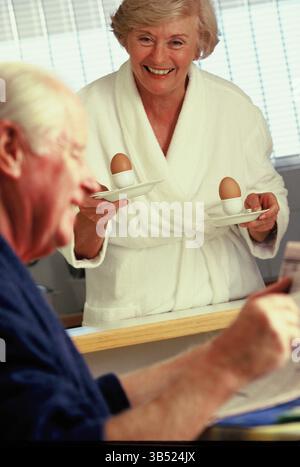 Senior couple in bathrobes indoors at home for boiled eggs breakfast. Stock Photo