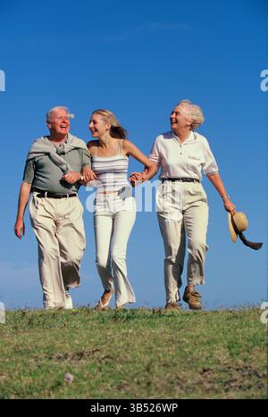 Senior couple with adult daughter walking outdoors on grassy hillside. Stock Photo