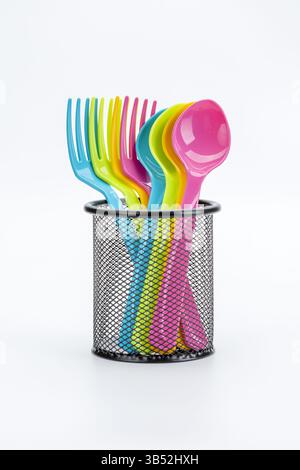 Colorful plastic cutlery stands in a sleek black holder, adding vibrant, cheerful contrast against a clean white background. Stock Photo