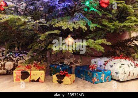 The bottom of a Christmas tree with presents wrapped in colorful paper and decorated with bows, placed on the floor. The tree is decorated with red an Stock Photo